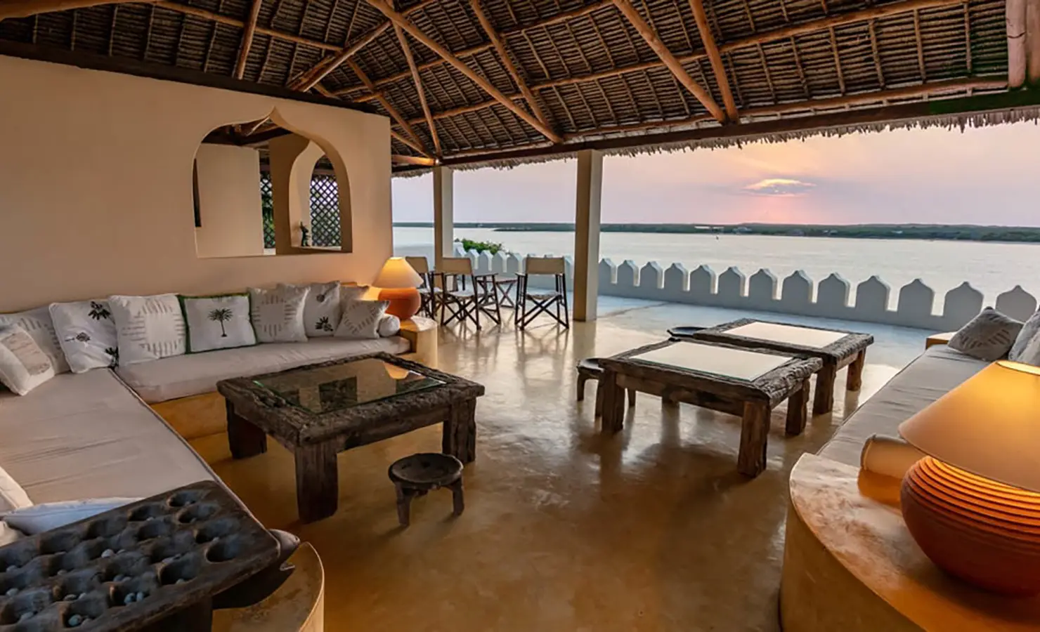 Perfect Hideaways: An open-plan living space with a rustic thatched roof, comfortable seating, and uninterrupted views of the ocean at sunset. Shela Beach House, Lamu.