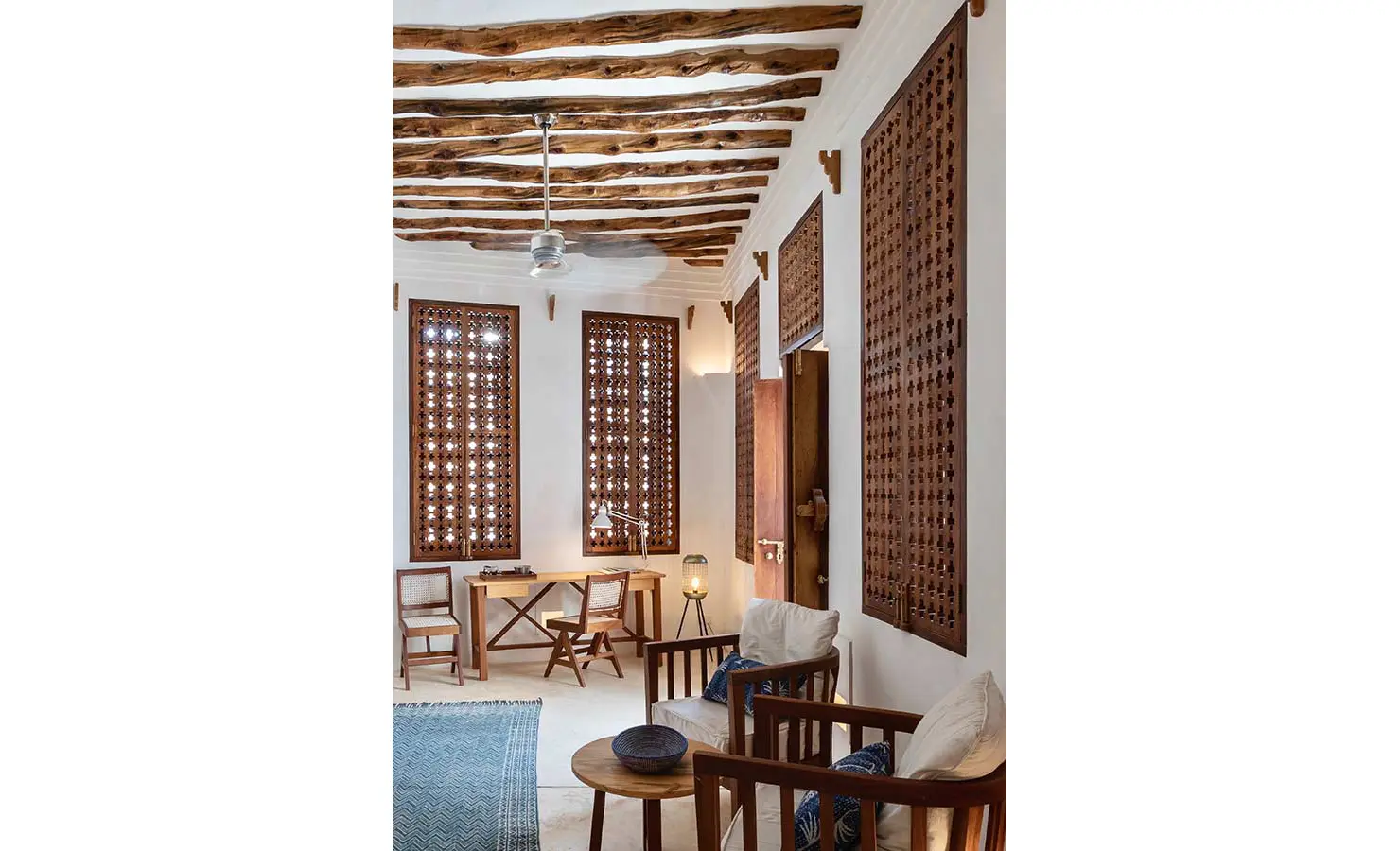 Perfect Hideaways: A cosy study room with wooden lattice windows, a writing desk, and chairs featuring rich wooden accents, illuminated by soft natural light. The Kasbah, Lamu.