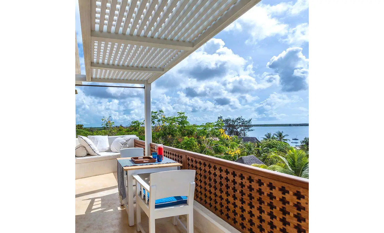 Perfect Hideaways: A rooftop terrace with a shaded seating area, white furnishings, and a panoramic view of lush greenery and the ocean in the distance. The Kasbah, Lamu.