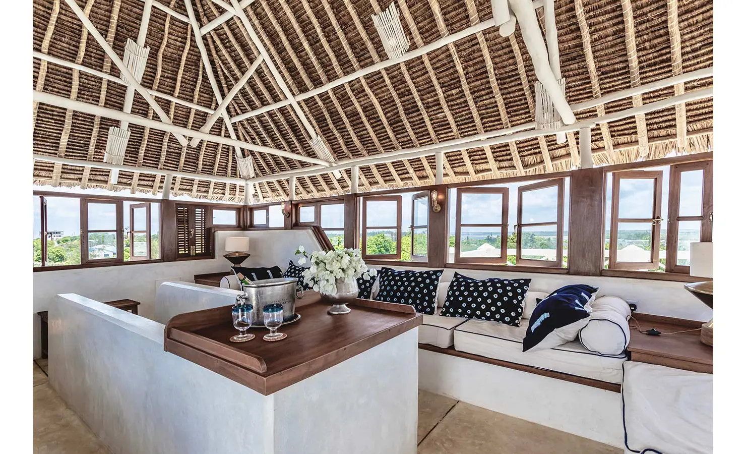 Perfect Hideaways: An airy rooftop lounge with a thatched ceiling, built-in seating, and wooden-framed windows offering sweeping views of the surroundings. The Kasbah, Lamu.