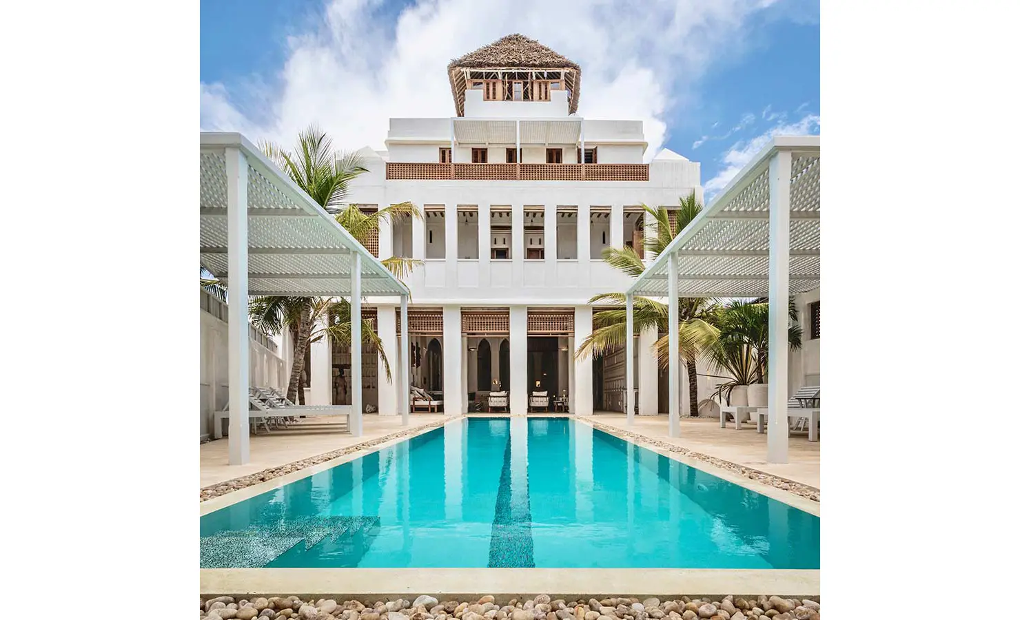 Perfect Hideaways: A luxurious white villa with traditional Swahili architectural elements, centred around a long blue-tiled pool lined with pergolas and palm trees. The Kasbah, Lamu.