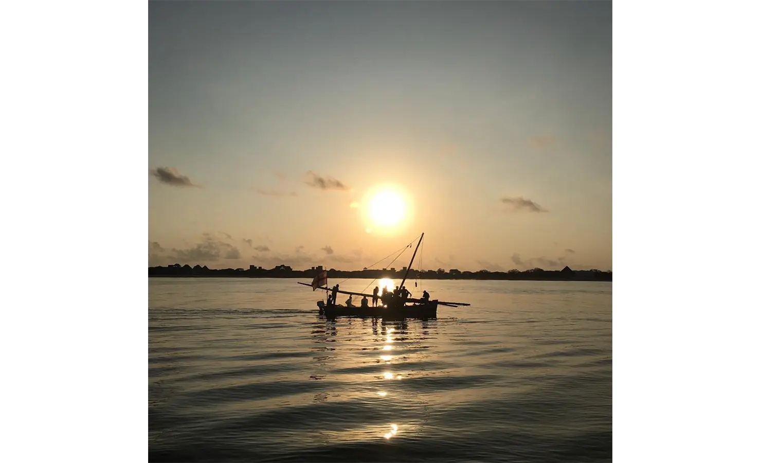 Perfect Hideaways: A dhow boat silhouetted against a stunning ocean sunset, with its reflection shimmering on the water's surface. Shela Beach House, Lamu.