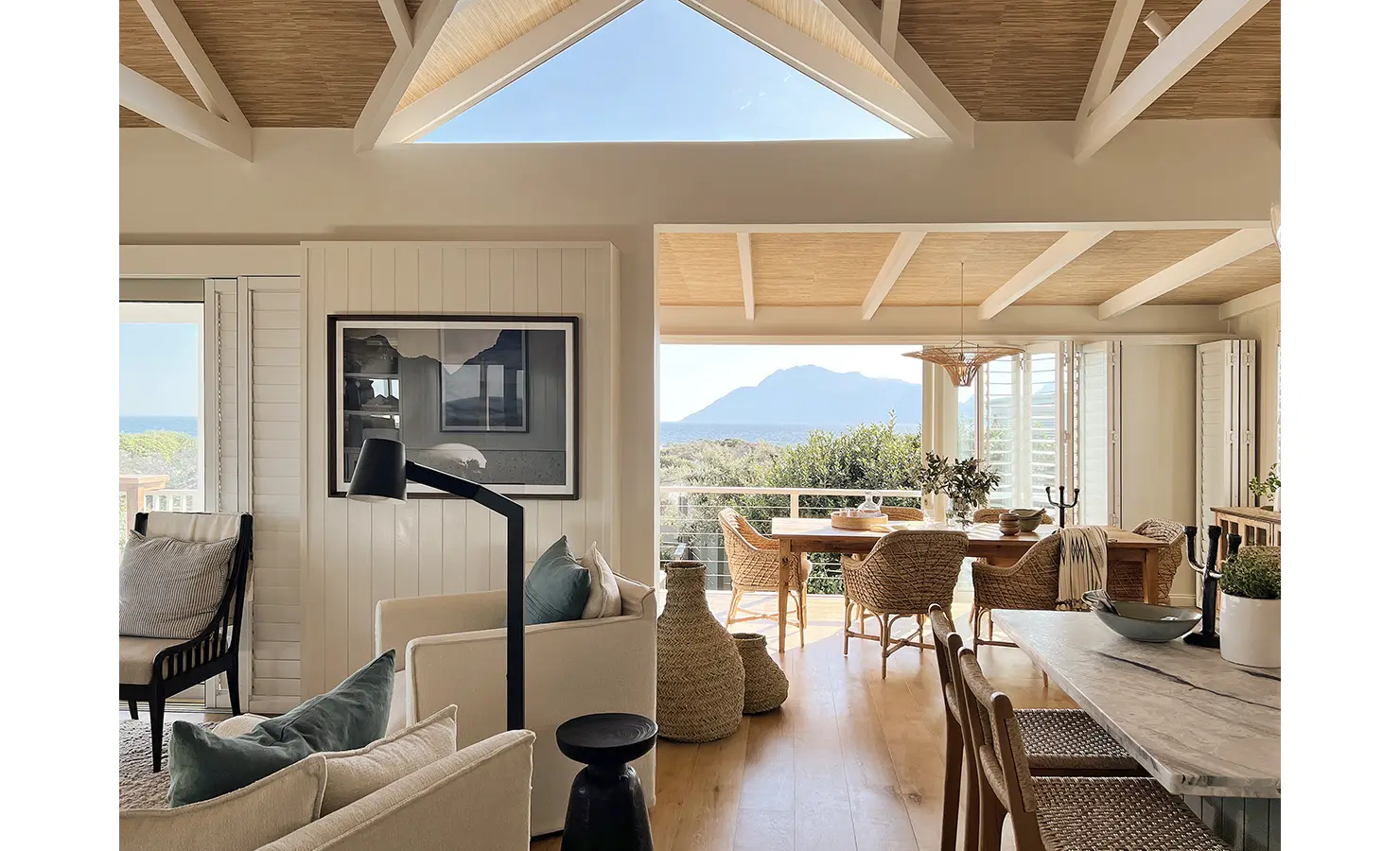 Perfect Hideaways: A seamless blend of indoor and outdoor living, this open-plan lounge flows effortlessly into a dining space with ocean views. High vaulted ceilings with exposed beams add to the airy, beach-inspired ambiance. Sunset Cove, Kommetjie.