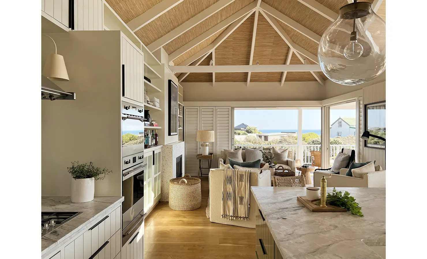 Perfect Hideaways: A sunlit kitchen with marble countertops, brass fixtures, and white cabinetry, blending timeless elegance with coastal charm. The open-plan design seamlessly connects to the living and dining areas. Sunset Cove, Kommetjie.