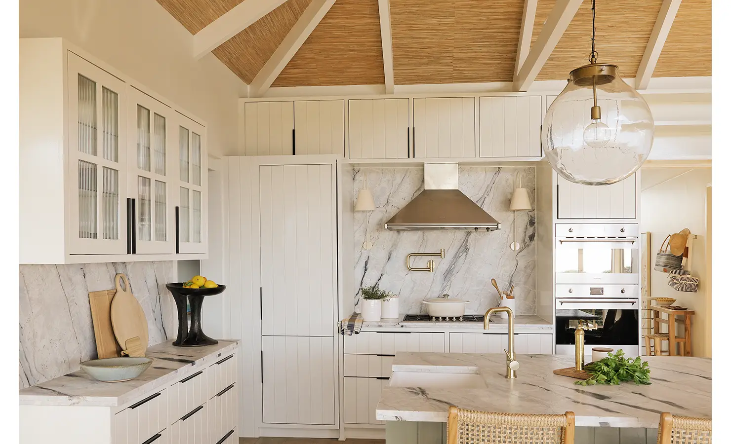 Perfect Hideaways: A bright and airy coastal kitchen with sleek cabinetry, marble detailing, and a spacious island. Glass pendant lighting and woven bar stools complete the relaxed yet refined aesthetic. Sunset Cove, Kommetjie.