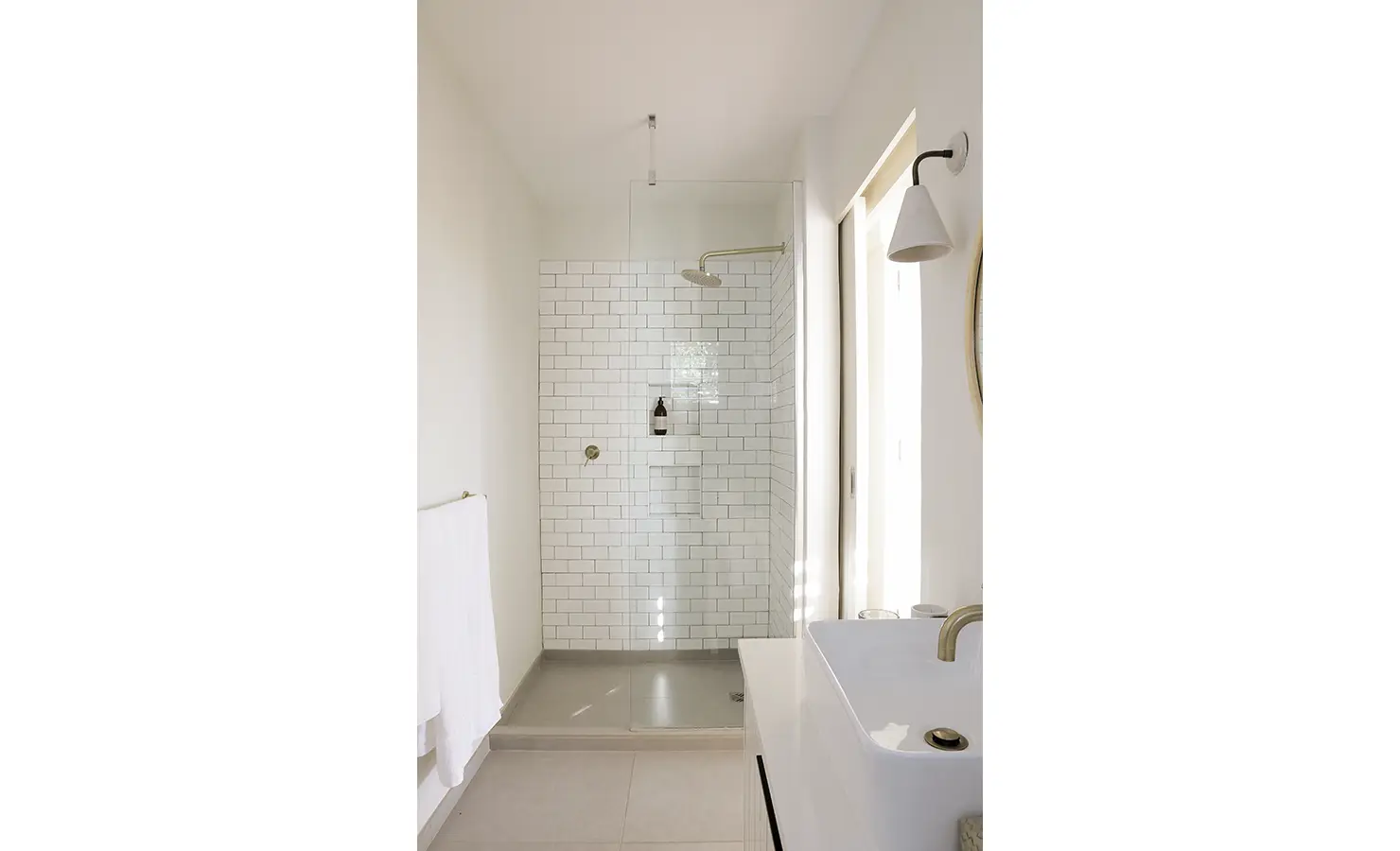 Perfect Hideaways: A minimalist bathroom with a glass-walled shower, white subway tiles, and brushed brass fixtures, exuding a fresh and airy feel. Sunset Cove, Kommetjie.