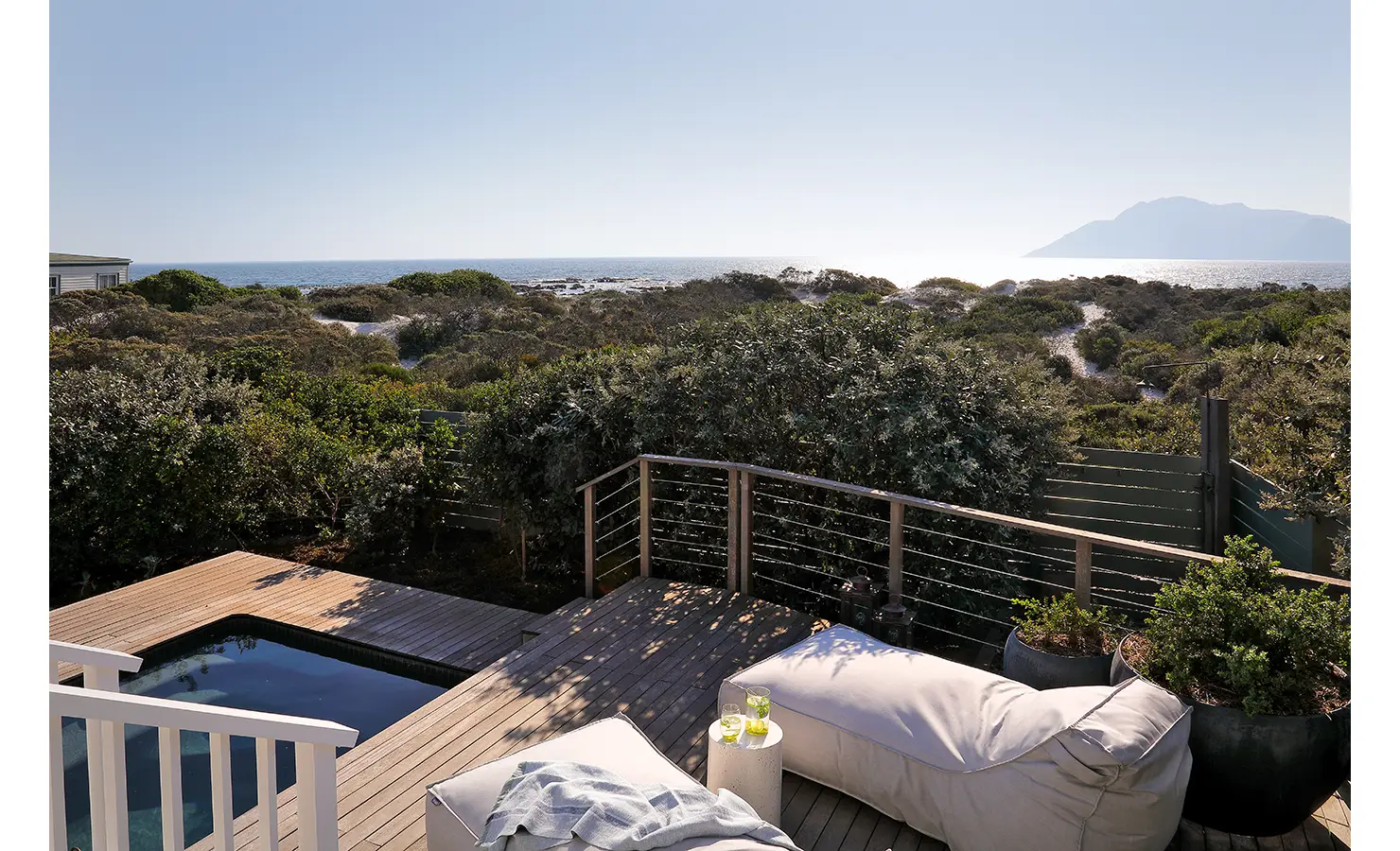 Perfect Hideaways: A private deck with an ocean-facing plunge pool, plush sun loungers, and lush indigenous greenery, offering the perfect setting to soak in coastal views. Sunset Cove, Kommetjie.