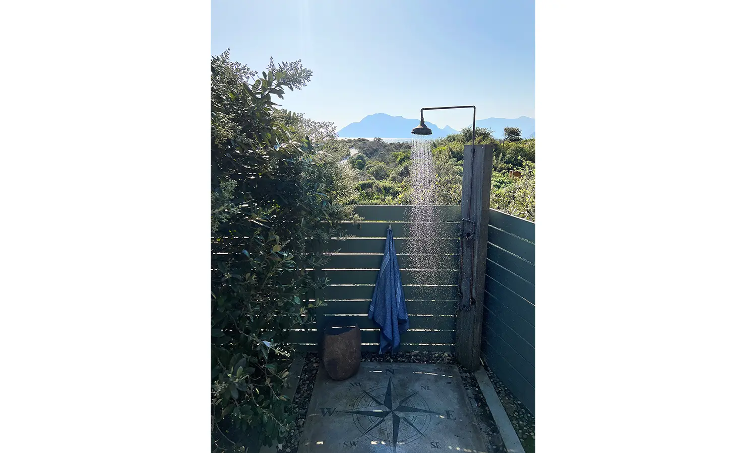 Perfect Hideaways: A secluded outdoor shower surrounded by lush foliage, with a simple wooden post and rainfall showerhead, providing a refreshing escape under the open sky. Sunset Cove, Kommetjie.