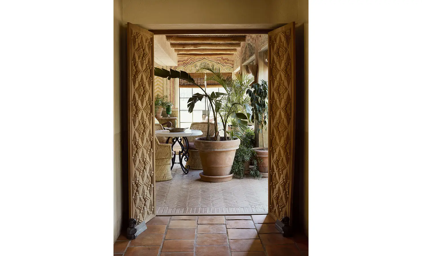 Perfect Hideaways: An intricately carved doorway leading to a bright patio adorned with potted plants and wicker furniture. Sterrekopje, Franschhoek.