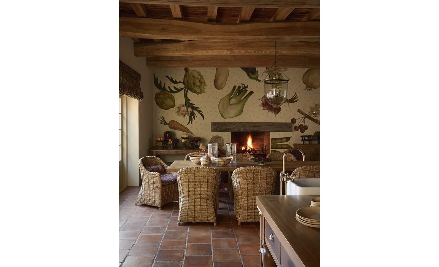 Perfect Hideaways: A kitchen with a rustic dining table surrounded by wicker chairs, complemented by a wall mural of vegetables and a warm fireplace. Sterrekopje, Franschhoek.