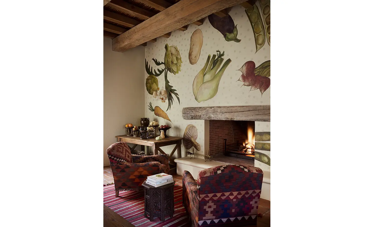 Perfect Hideaways: A snug sitting area featuring colourful upholstered chairs, a patterned rug, and a fireplace with a vegetable mural in the background. Sterrekopje, Franschhoek.