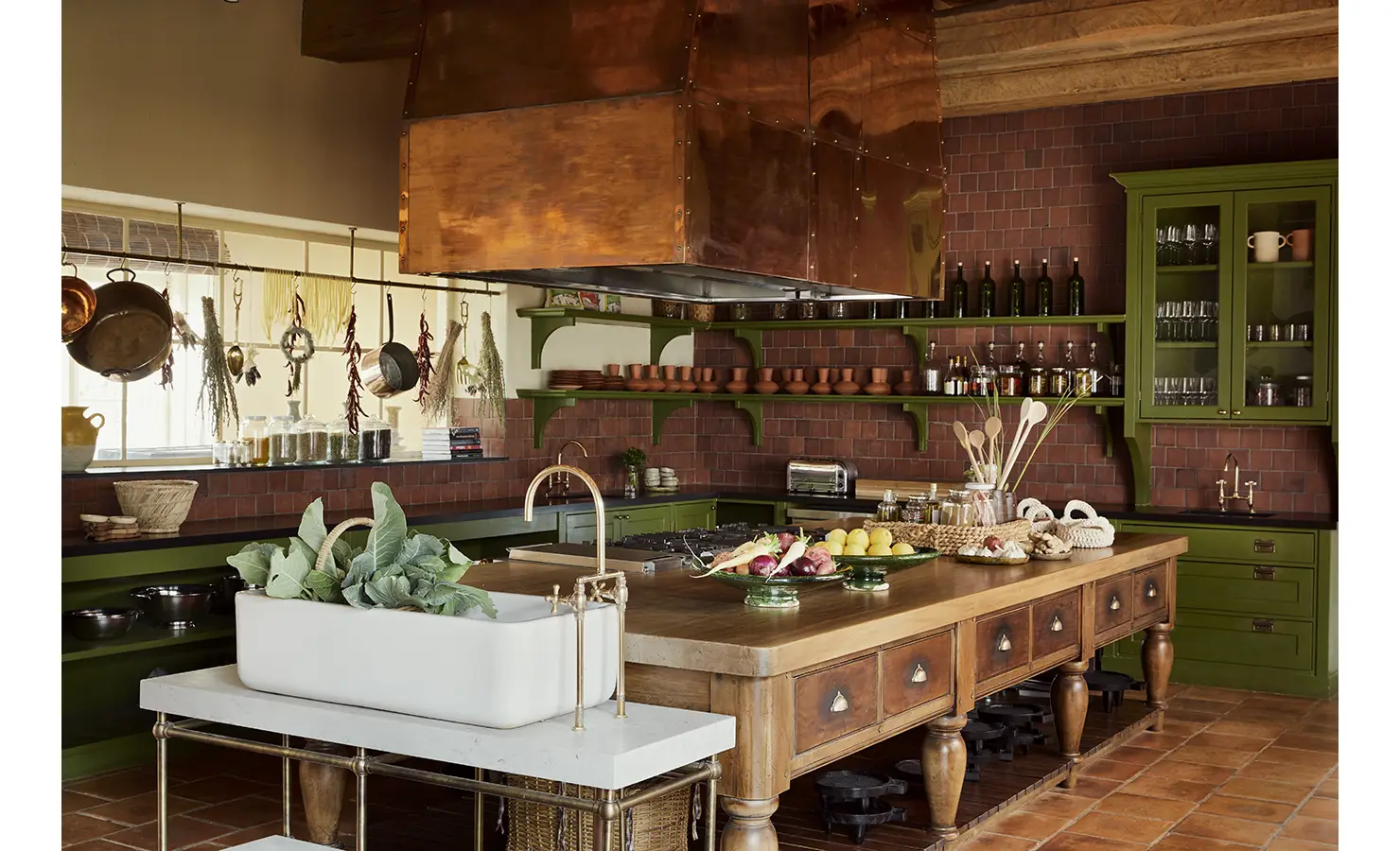 Perfect Hideaways: A rustic kitchen with green cabinets, open shelves displaying pottery, a large copper hood, and a central wooden island adorned with fresh produce. Sterrekopje, Franschhoek.