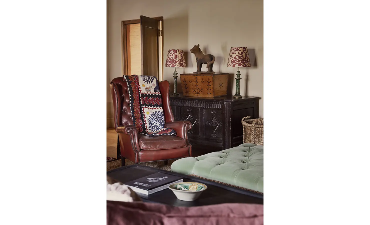 Perfect Hideaways: A close-up of a leather armchair with a colourful throw, placed next to an ornate black cabinet topped with unique lamps and decor. Sterrekopje, Franschhoek.