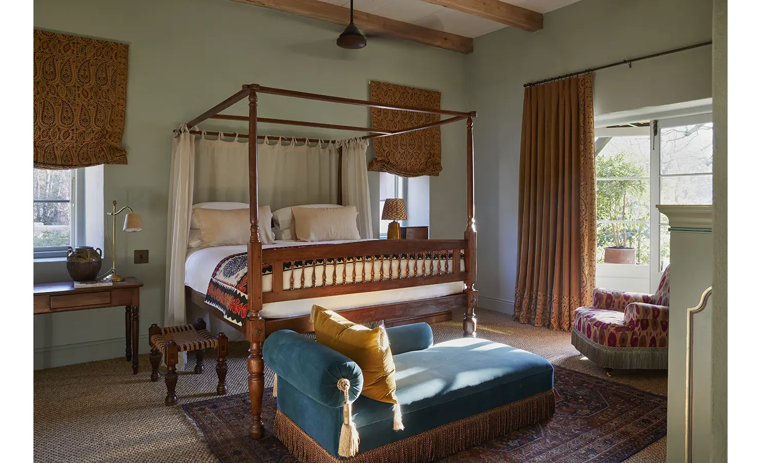 Perfect Hideaways: A serene bedroom with a four-poster bed draped in soft curtains, a teal chaise lounge, and warm light streaming through the windows. Sterrekopje, Franschhoek.