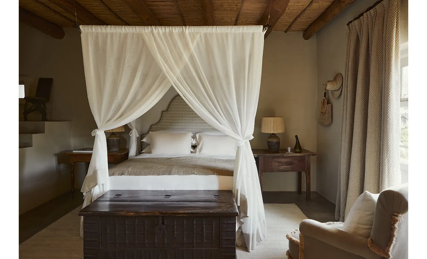Perfect Hideaways: A romantic bedroom with a canopy bed draped in white fabric, wooden accents, and a rustic chest at the foot of the bed. Sterrekopje, Franschhoek.