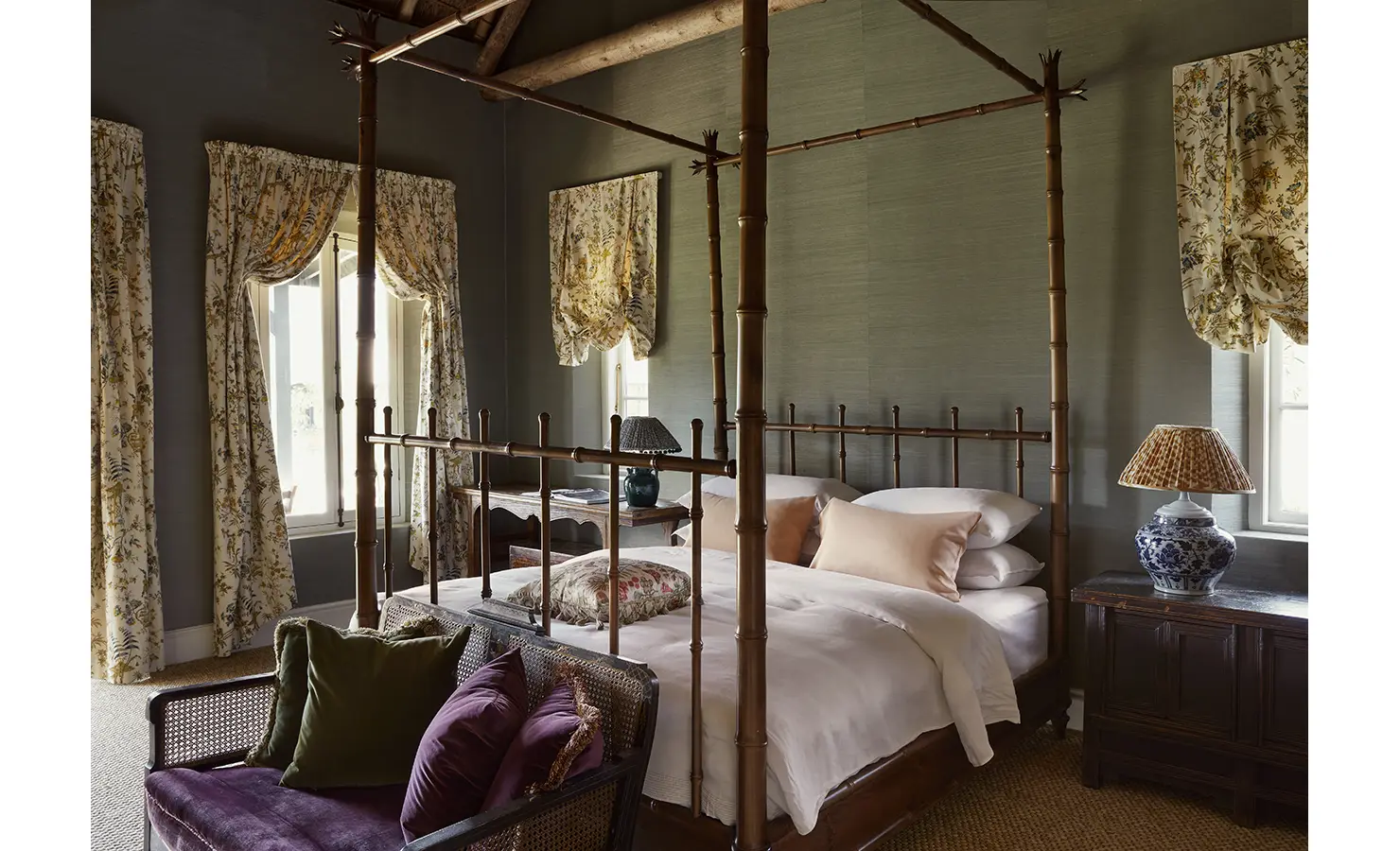 Perfect Hideaways: A bedroom featuring a bamboo-style four-poster bed with floral drapes, elegant side tables, and plush seating. Sterrekopje, Franschhoek.