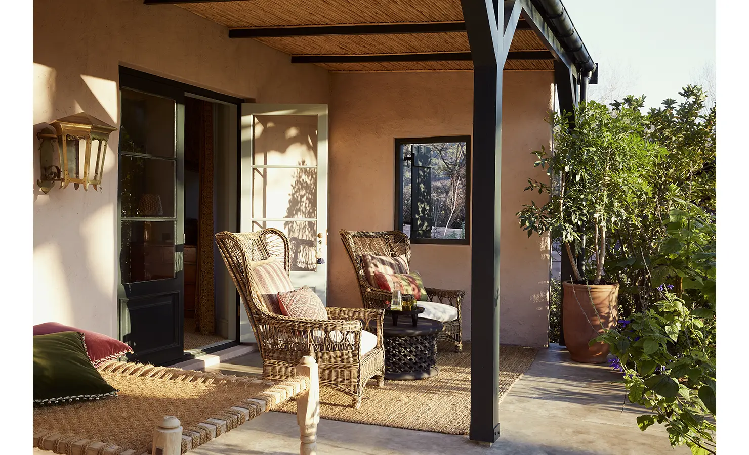 Perfect Hideaways: A charming outdoor patio with wicker chairs, potted plants, and a thatched awning, bathed in soft natural light. Sterrekopje, Franschhoek.