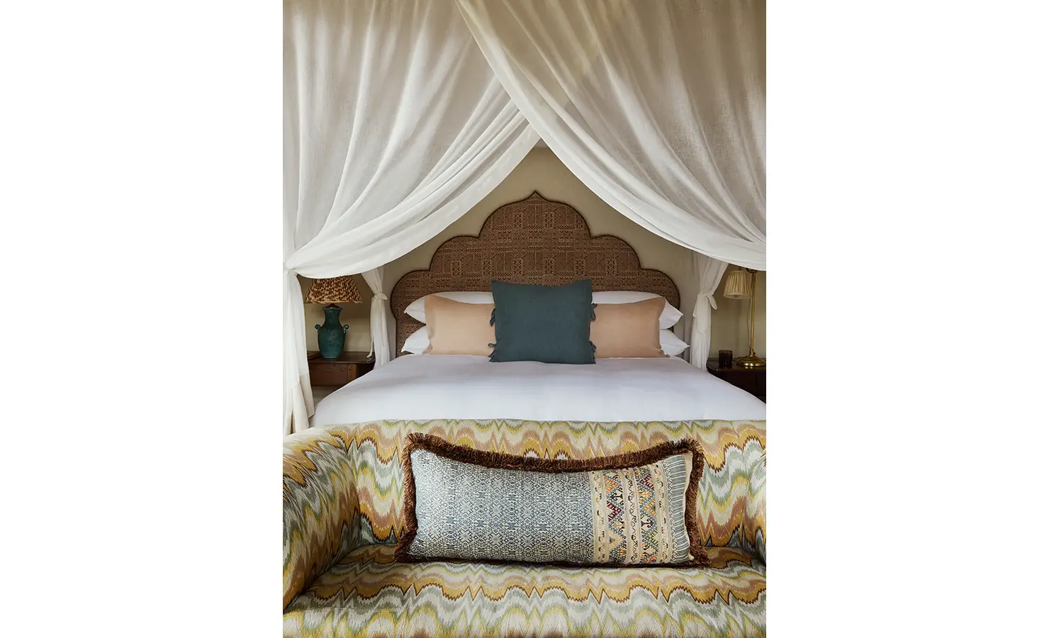 Perfect Hideaways: A close-up of a canopied bed with ornate detailing, flanked by elegant lamps and soft, textured cushions. Sterrekopje, Franschhoek.