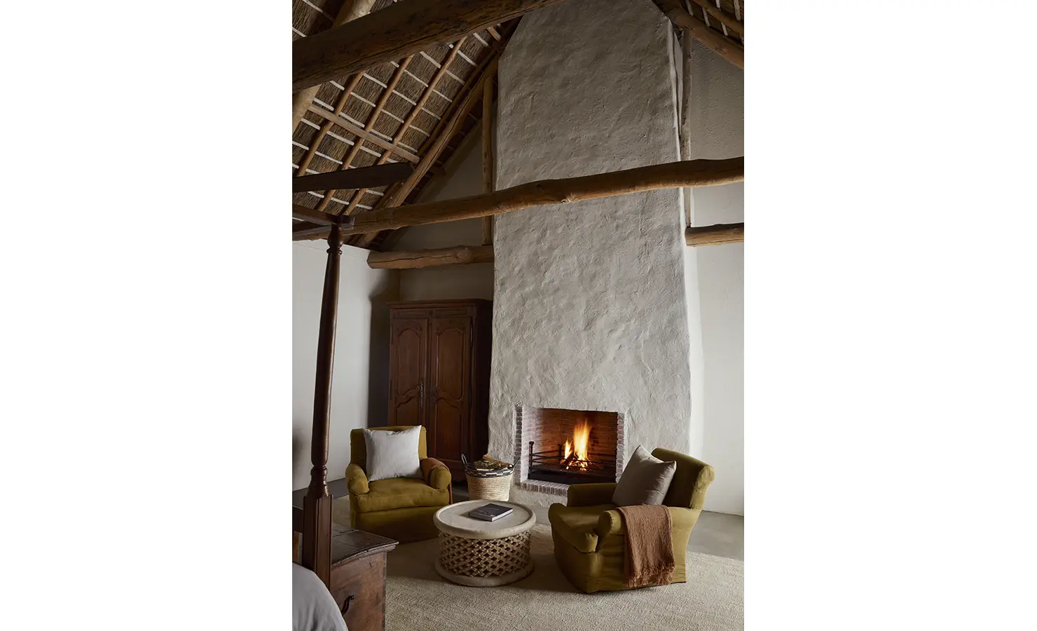 Perfect Hideaways: A cosy seating area in front of a rustic fireplace, featuring two plush armchairs and a round woven table. Sterrekopje, Franschhoek.