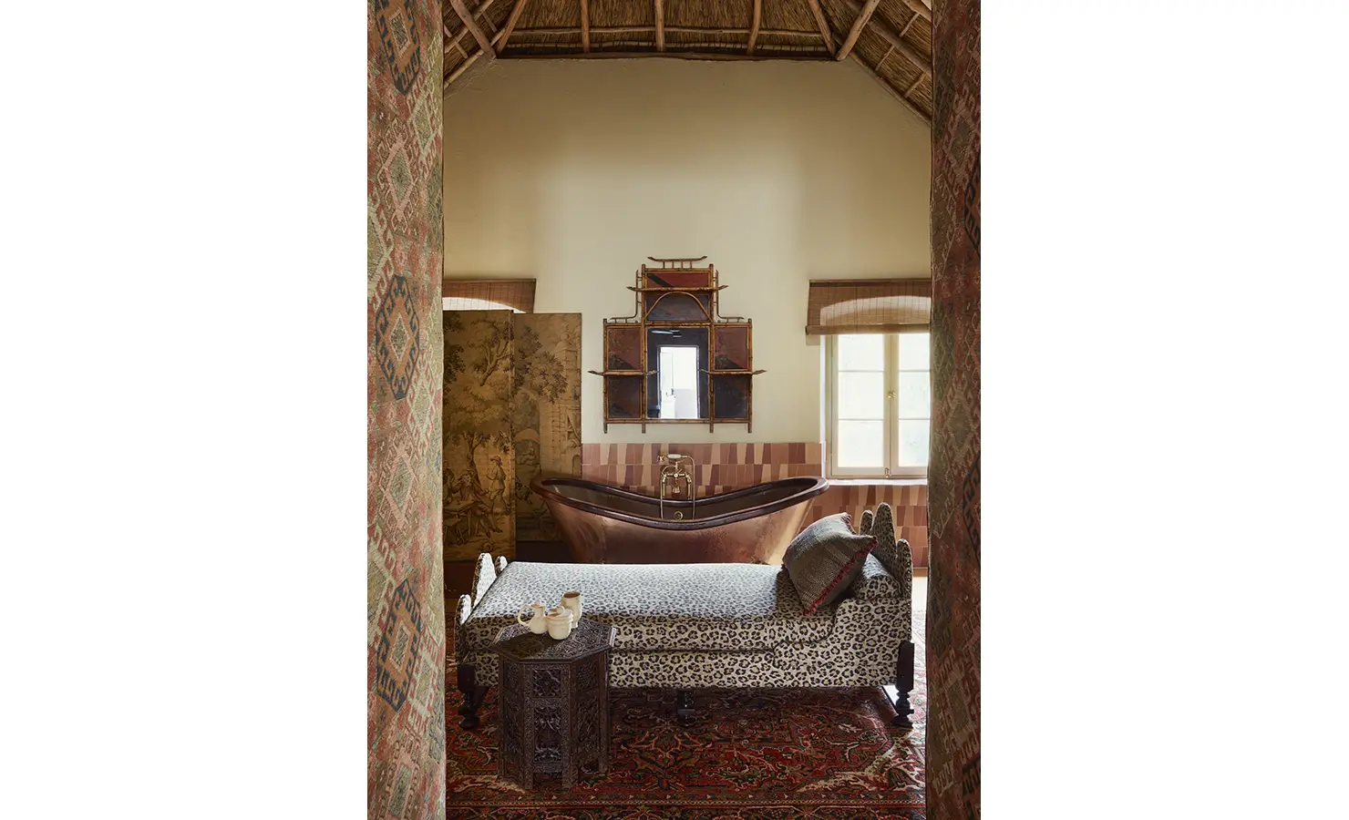 Perfect Hideaways: A luxurious bathroom featuring a copper bathtub, a decorative screen, and a chaise lounge with intricate textiles. Sterrekopje, Franschhoek.