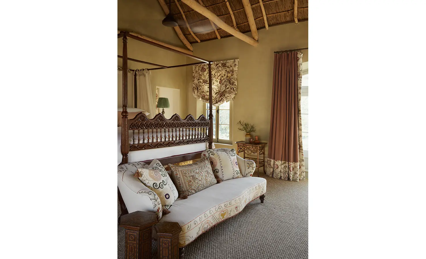 Perfect Hideaways: A light-filled bedroom with a carved four-poster bed, floral curtains, and a delicate sofa with embroidered cushions. Sterrekopje, Franschhoek.