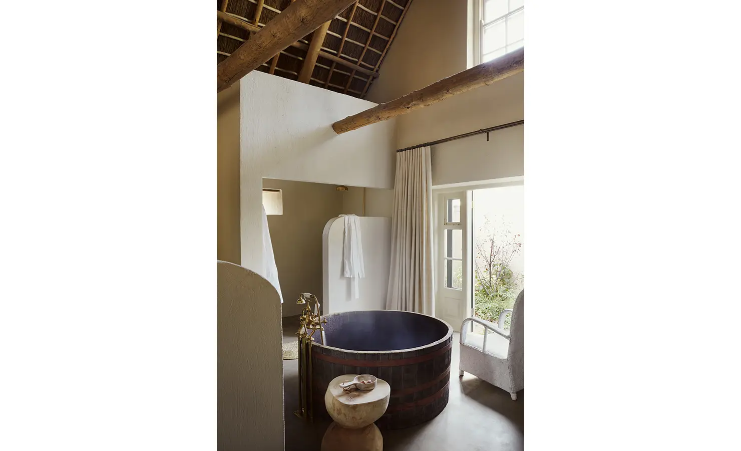 Perfect Hideaways: A bathroom with a circular wooden tub, soft lighting, and large windows opening onto a private garden. Sterrekopje, Franschhoek.