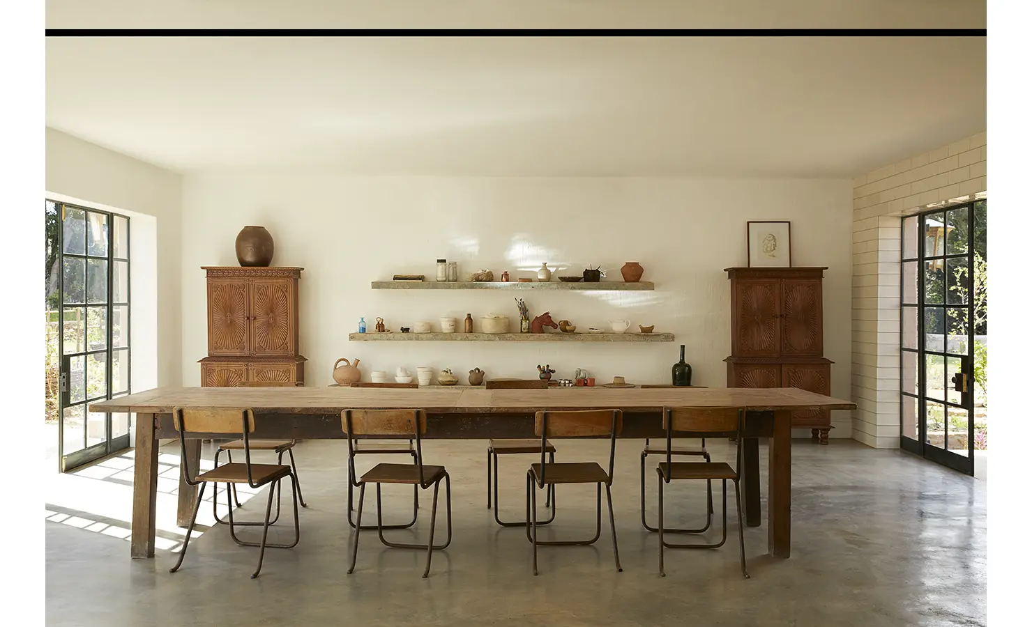 Perfect Hideaways: A minimalist dining space featuring a long rustic table, industrial-style chairs, and natural light streaming through glass-panelled doors. Sterrekopje, Franschhoek.
