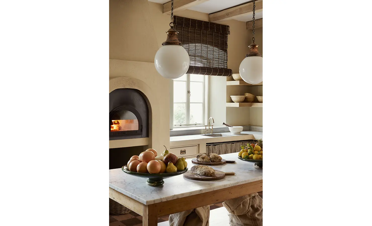 Perfect Hideaways: A rustic kitchen with a wood-fired oven, marble-topped island, and bowls of fresh produce, illuminated by warm pendant lighting. Sterrekopje, Franschhoek.