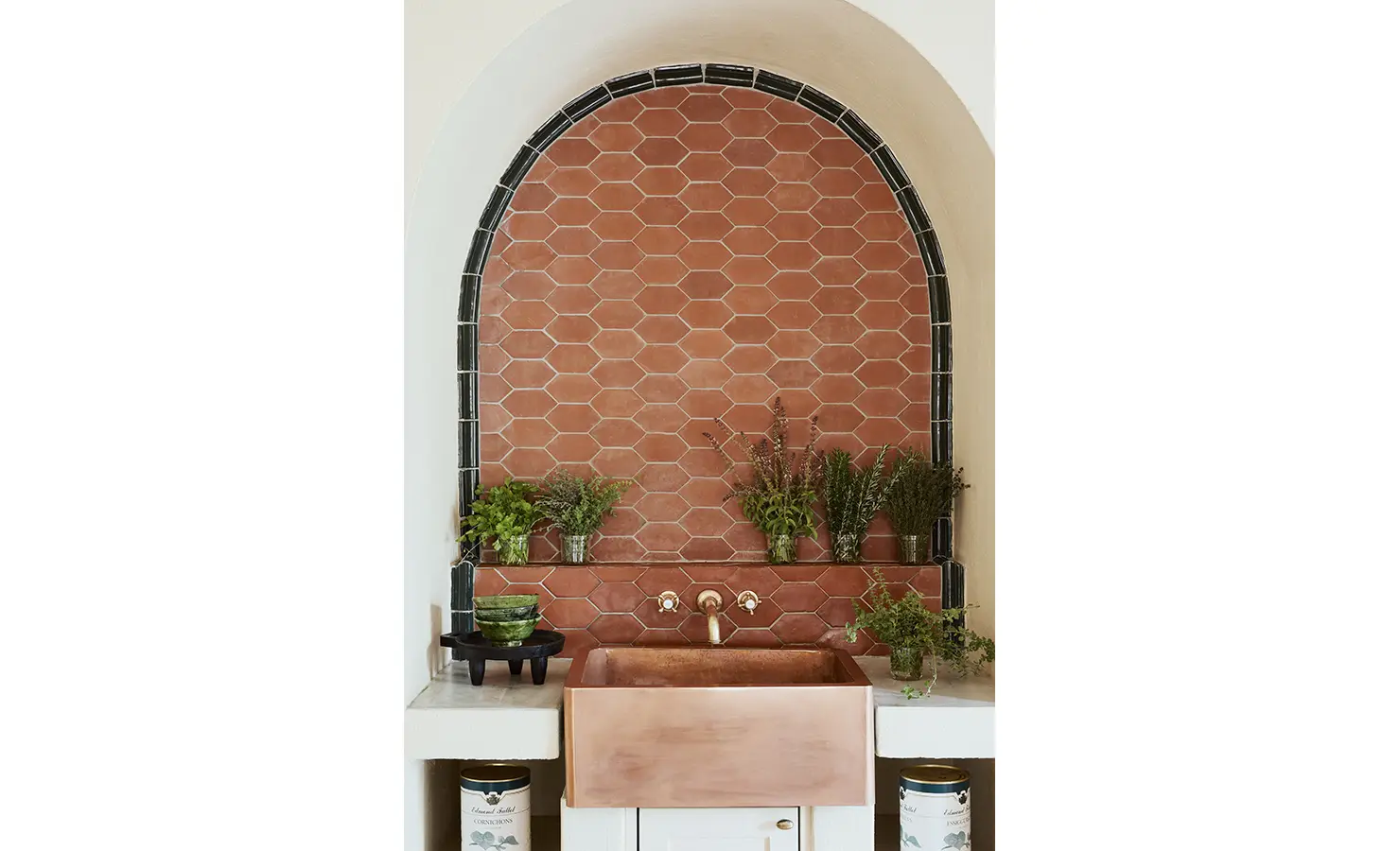 Perfect Hideaways: A terracotta kitchen backsplash with a copper sink, framed by an arched niche and decorated with fresh herbs in glass jars. Sterrekopje, Franschhoek.