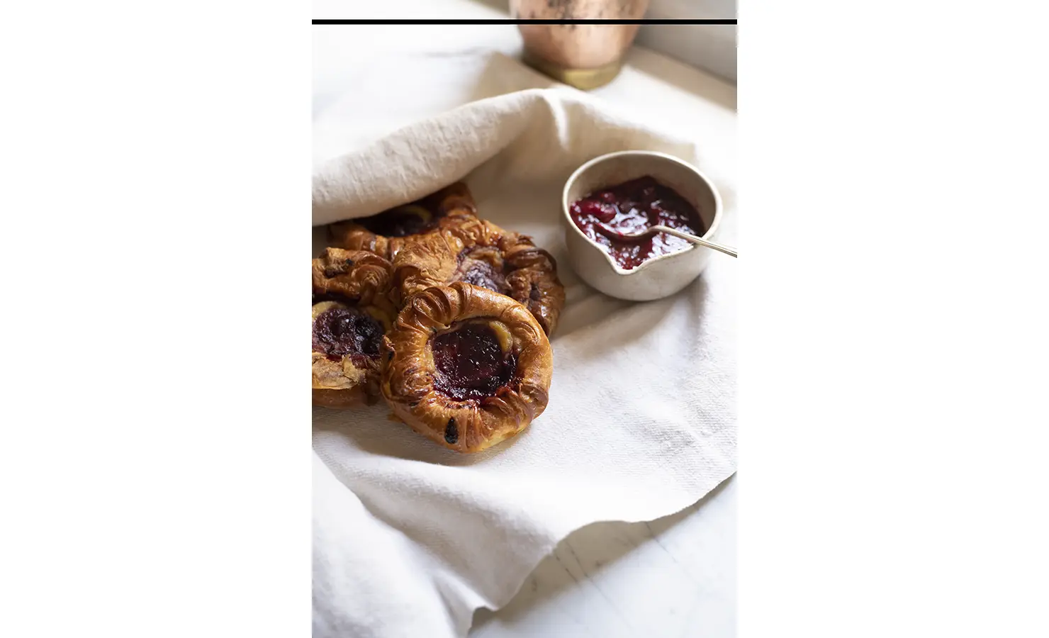 Perfect Hideaways: A close-up of flaky pastries filled with berry compote, accompanied by a bowl of vibrant red jam on a soft linen cloth. Sterrekopje, Franschhoek.