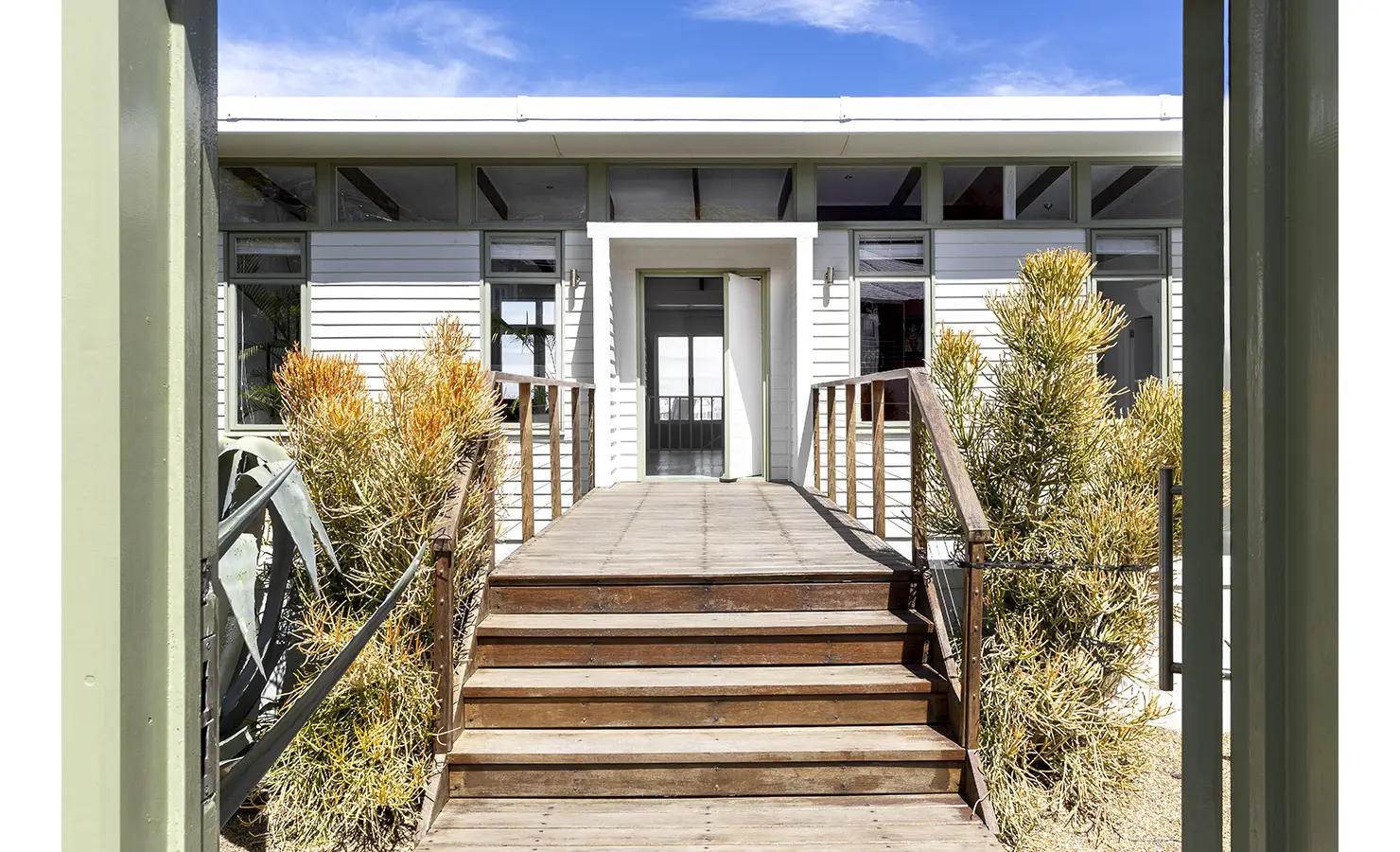 Perfect Hideaways private entrance with wooden steps and railing leading to a light grey beach-style home surrounded by indigenous plants under a bright blue sky, Summer Rose, Camps Bay