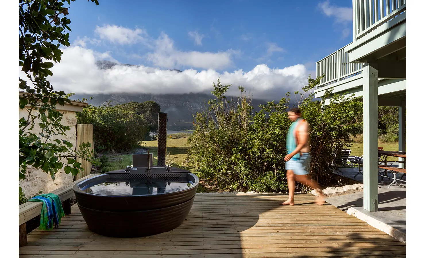 Perfect Hideaways: Wood-fired hot tub on a timber deck with mountain clouds spilling over the ridge beside mint-painted balconies, Stanford, Coot Club.