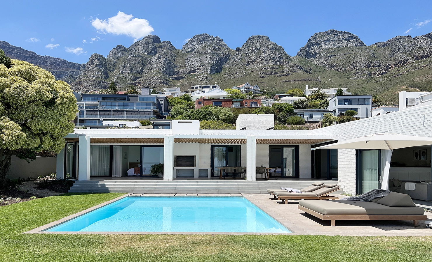 Perfect Hideaways: A modern, minimalist villa with a pristine swimming pool, sun loungers, and an expansive outdoor living area, set against the dramatic backdrop of the Twelve Apostles mountain range in Camps Bay. House Jack, Camps Bay.