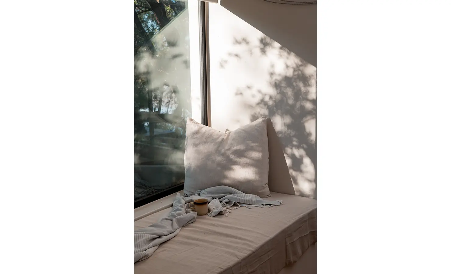 Perfect Hideaways: A tranquil window seat bathed in dappled sunlight offers a peaceful spot for relaxation. A soft throw and a steaming cup of tea complete this serene riverside escape. Orange River House, Hopetown.