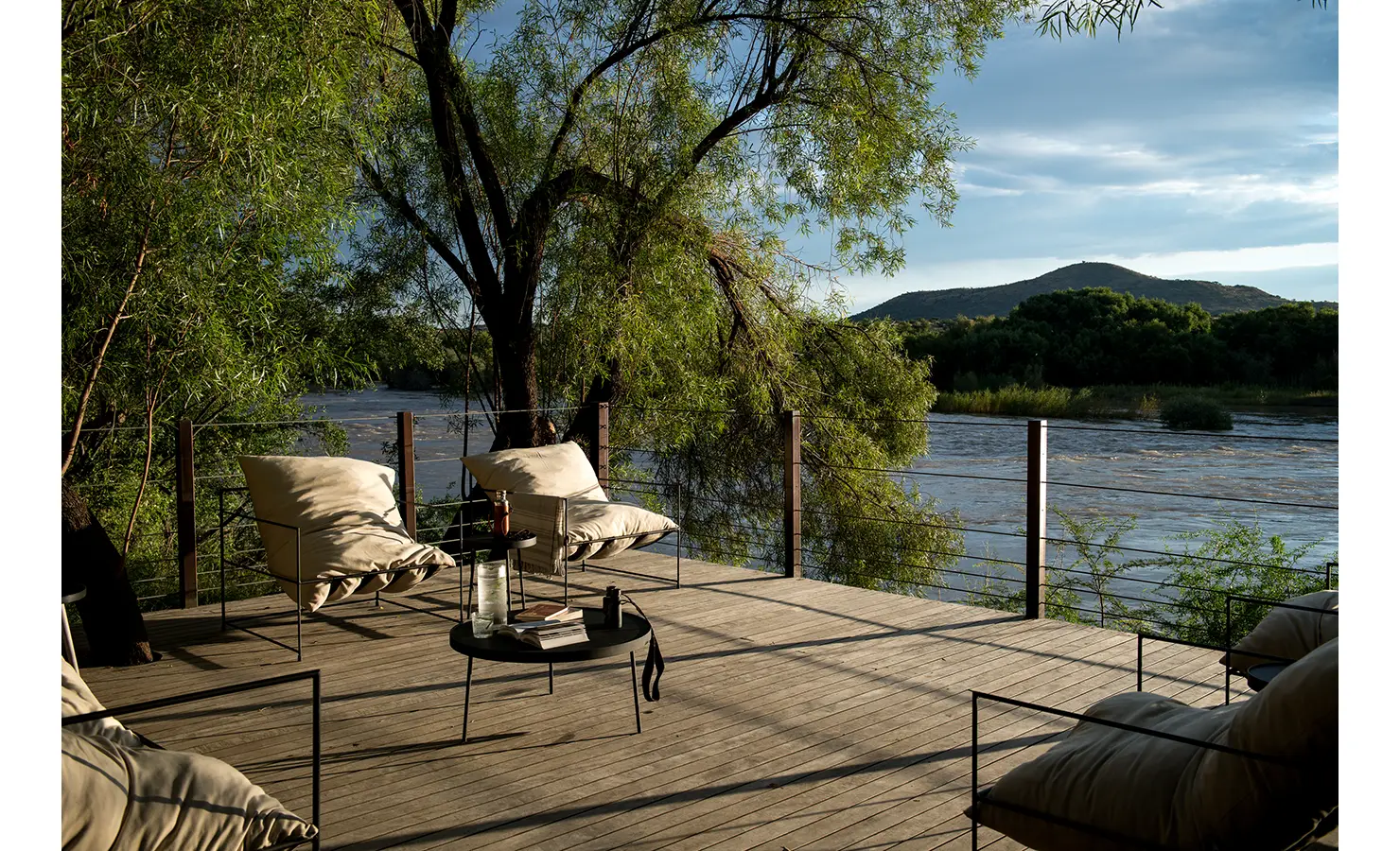 Perfect Hideaways: A riverside deck with plush lounge chairs offers a serene retreat, where guests can unwind with panoramic views of the flowing Orange River and distant hills. Orange River House, Hopetown.