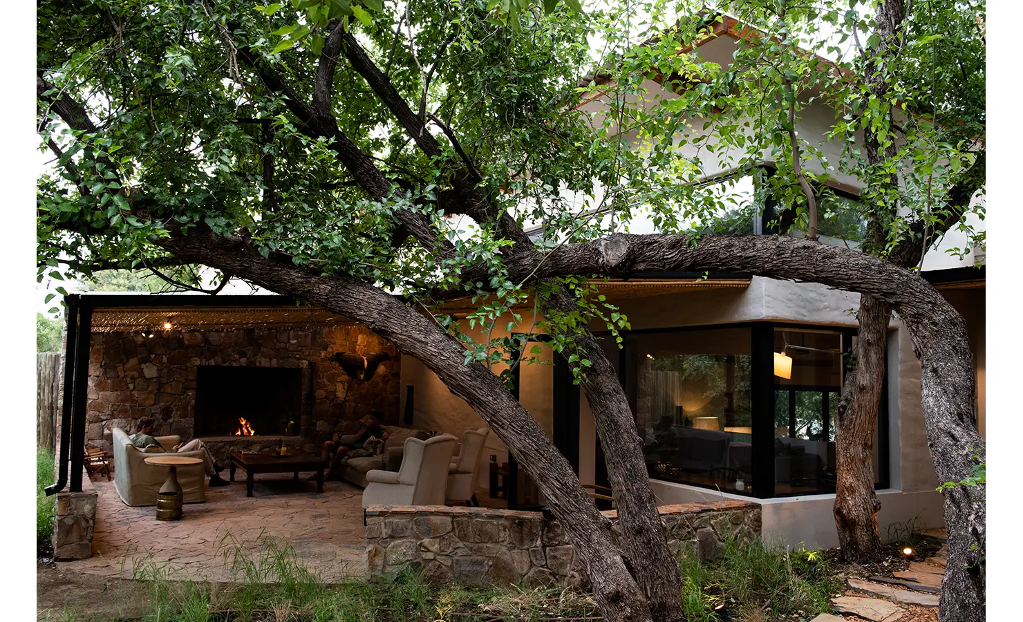 Perfect Hideaways: A beautifully designed home nestles among mature trees, with a stone-clad outdoor lounge and fireplace providing a warm and inviting retreat amidst nature. Orange River House, Hopetown.