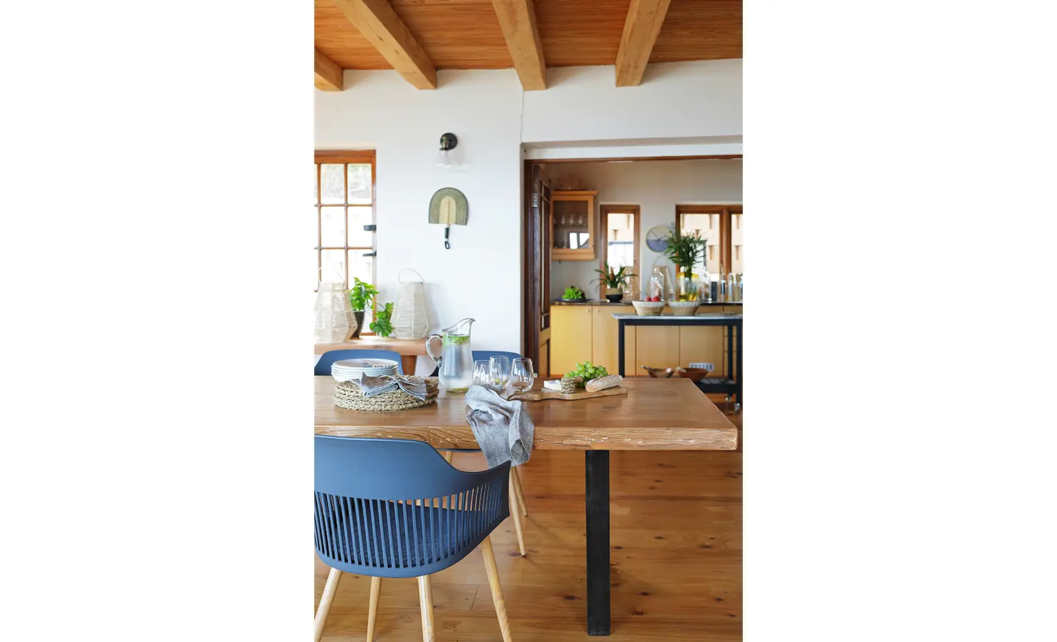 Perfect Hideaways: Side view of dining room table with kitchen shown behind. Wooden flooring, table tops and ceiling shown throughout the home. Sefarina, Noordhoek.