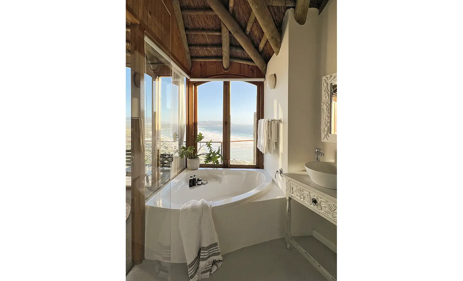 Perfect Hideaways: The master bathtub situated in the corner of the bathroom. Pale white colours and views of the beach. Sefarina, Noordhoek.