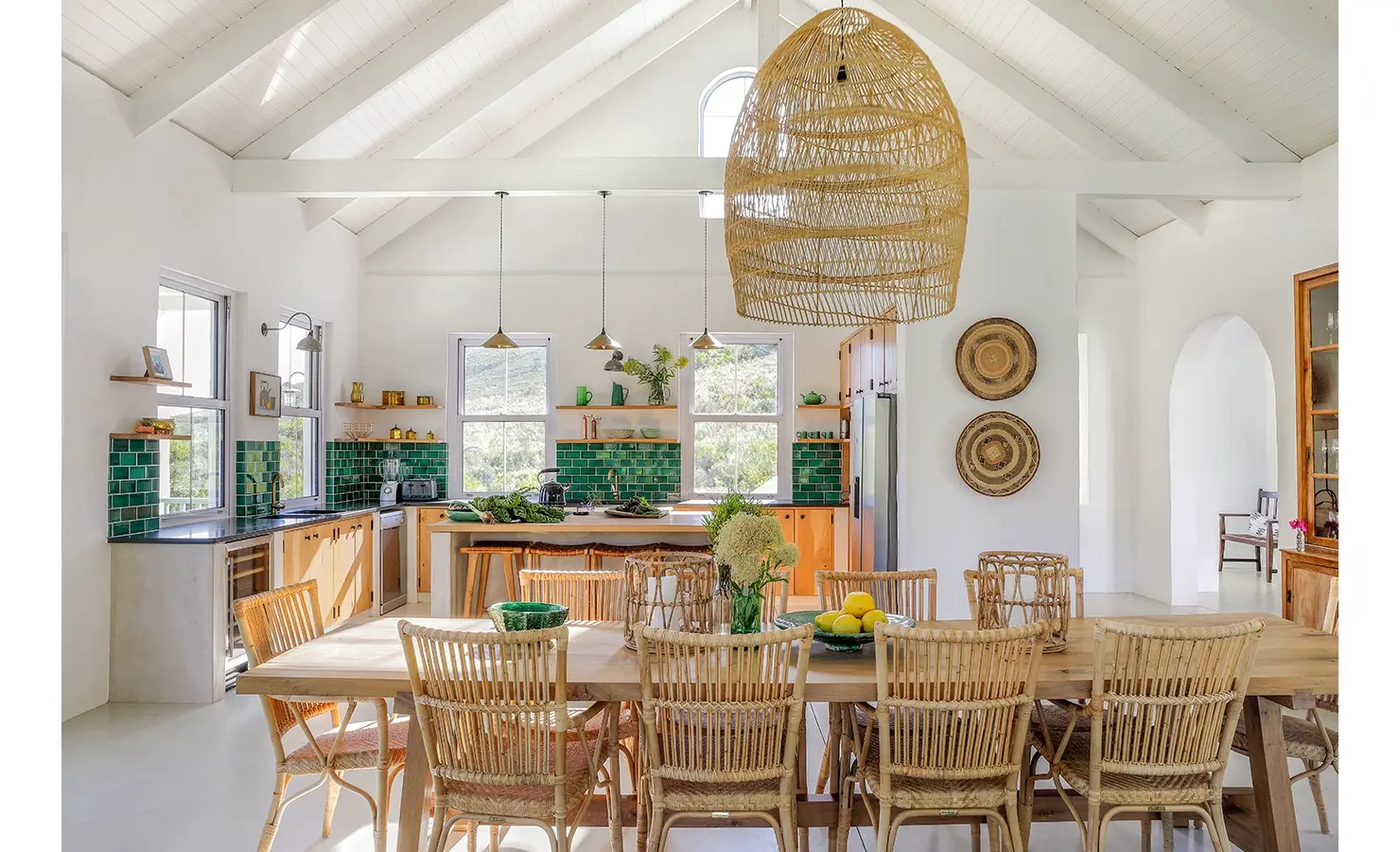 Natural hues of Banghoek Nature Reserve reflecting in the long wooden dining table and chairs, the green tiled kitchen walls and wooden cabinets, and the surrounding decor.