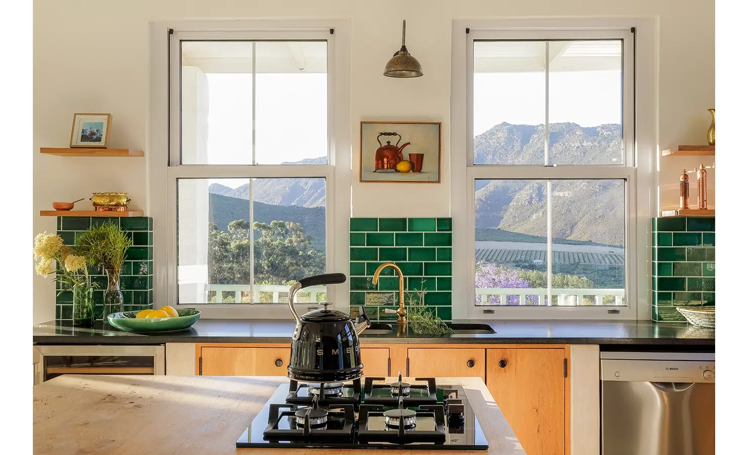 Kitchen island with built in gas stove and facing the green tiled walls with two large windows exposing the mountainous landscape. Buchubos Villa.
