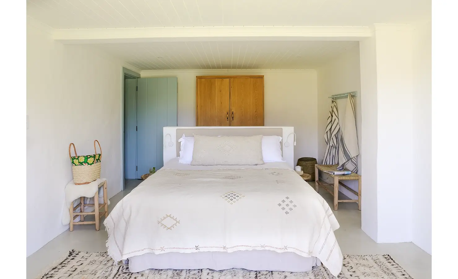 Spacious bed with beige linen bedding that match the flooring, a wooden cabinet and blue wooden door.