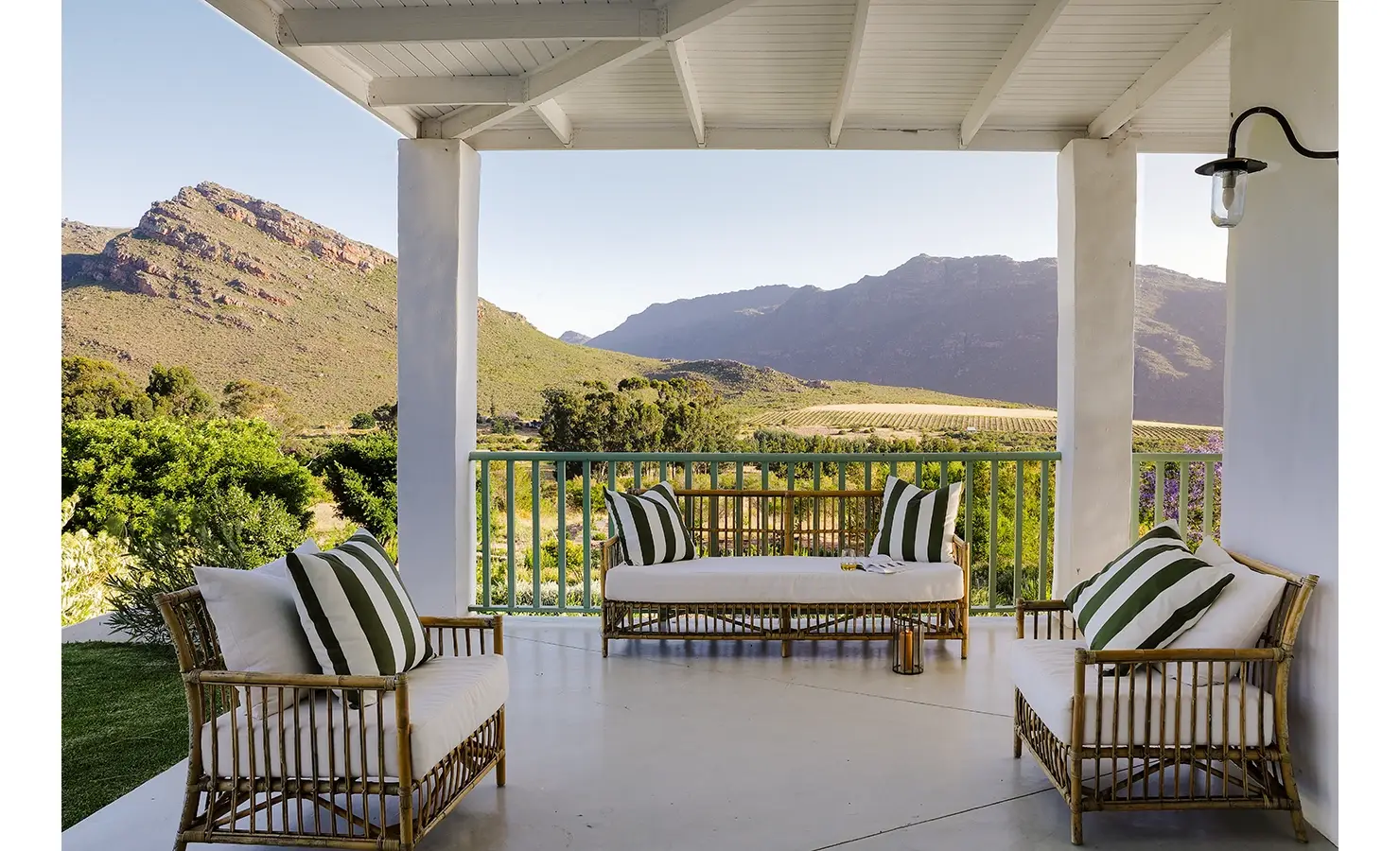 Wrap around verandah at Buchubos Villa with white cushioned wicker sofa and armchairs overlooking the luscious landscape and surrounding mountain range.