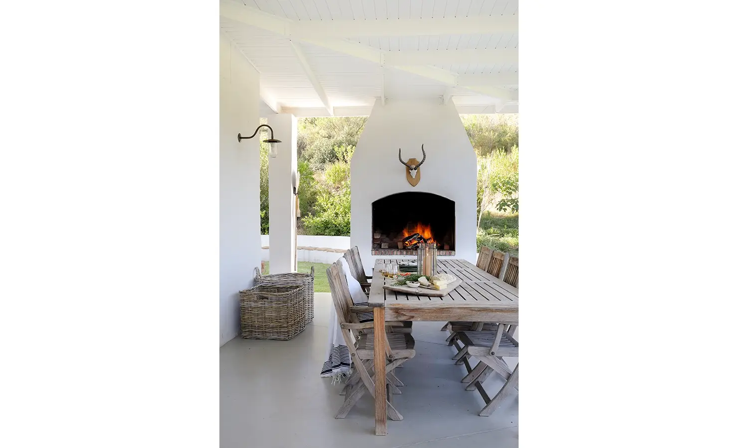 Outdoor braai area with long wooden table and chairs protected by an elongated roof. Buchubos villa.