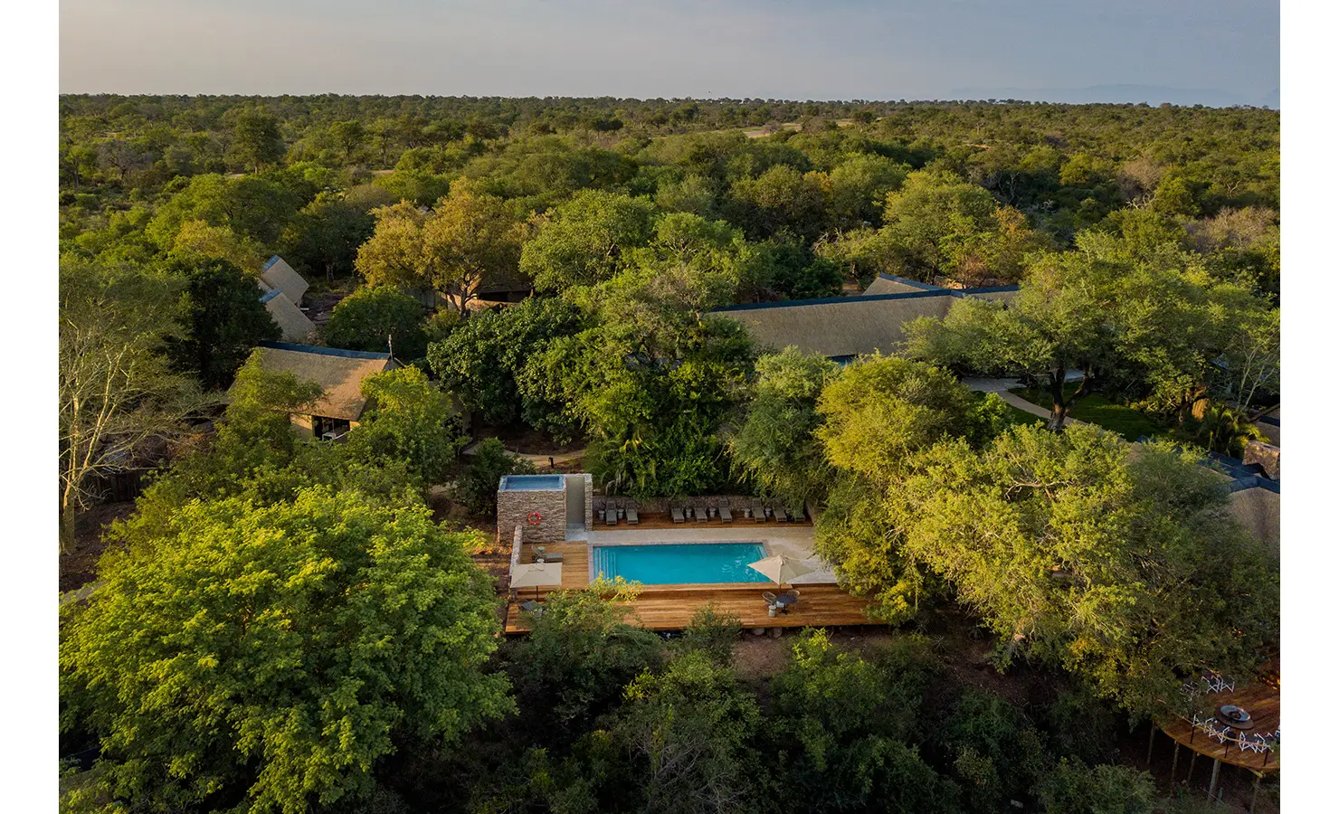 Perfect Hideaways: A stunning aerial shot of Thornybush Lodge, nestled amidst the verdant landscape of the reserve. Raised wooden decks with elegant seating areas extend over the sandy riverbed, offering breathtaking panoramic views of the untamed wilderness. Thornybush Lodge, Thornybush Game Reserve.