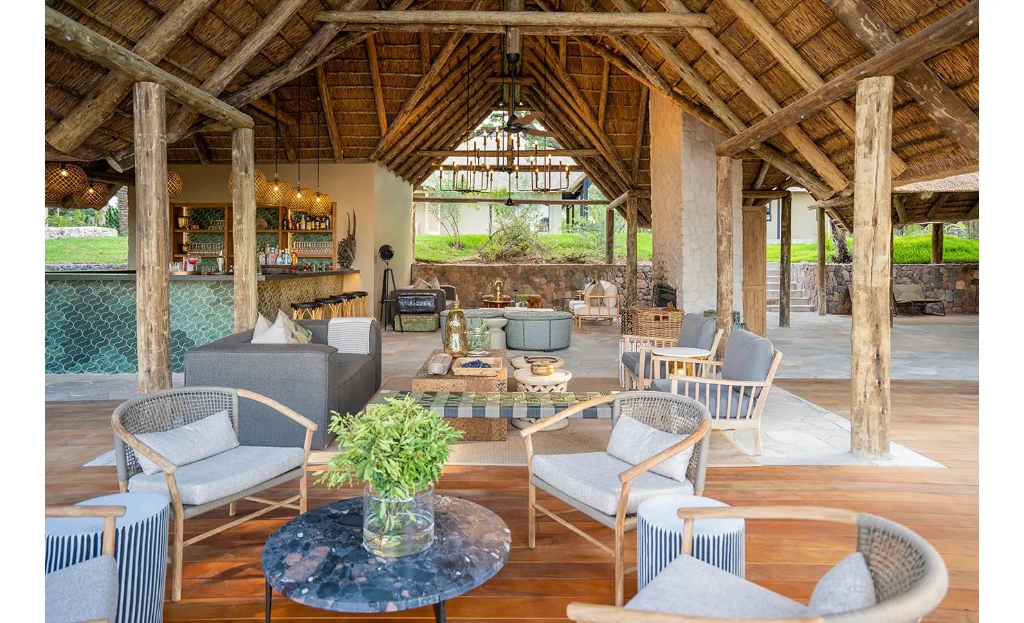 Perfect Hideaways: The welcoming open-air lounge at Thornybush Lodge, featuring rustic stone flooring, high thatched ceilings, and elegant furnishings. Large archways frame views of the lush landscape, inviting the outdoors in. Thornybush Lodge, Thornybush Game Reserve.