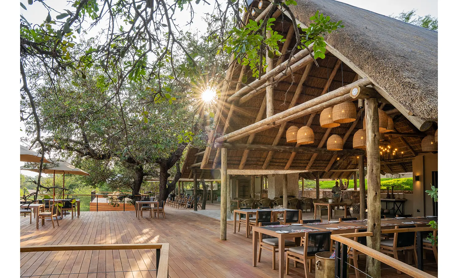Perfect Hideaways: The beautifully designed main lounge and bar area, featuring comfortable sofas, tufted ottomans, and striking chandeliers. Large glass doors open onto an expansive deck, seamlessly blending indoor and outdoor living. Thornybush Lodge, Thornybush Game Reserve.