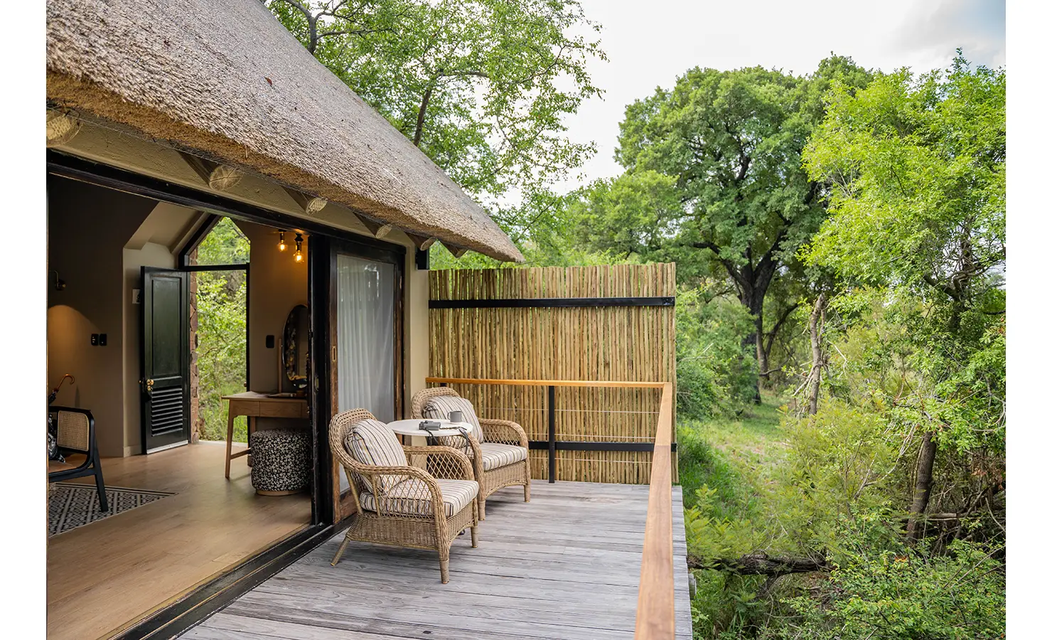 Perfect Hideaways: A serene private suite with a thatched roof, vibrant patterned decor, and a shaded outdoor sitting area. Large sliding doors offer seamless indoor-outdoor living. Thornybush Lodge, Thornybush Game Reserve.
