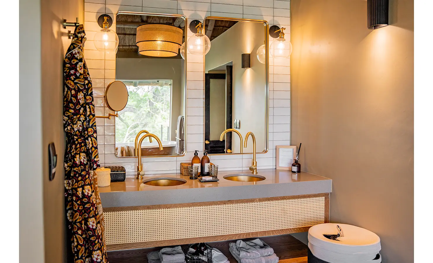 Perfect Hideaways: A luxurious bathroom featuring a freestanding bathtub with brass fixtures, patterned floor tiles, and floor-to-ceiling glass windows that offer an uninterrupted view of the wilderness. Thornybush Lodge, Thornybush Game Reserve.