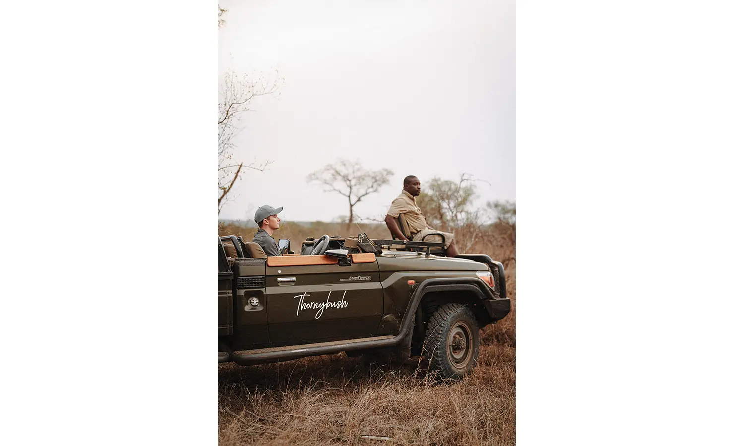 Perfect Hideaways: A safari vehicle at Thornybush Lodge, where a guide and tracker scan the surroundings for wildlife. The rugged Land Cruiser, marked with the Thornybush logo, is designed for immersive game drives in the African bush. Thornybush Lodge, Thornybush Game Reserve.