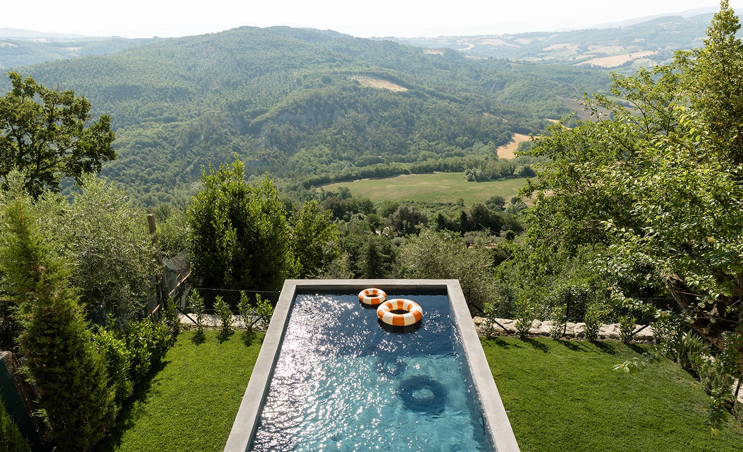 Perfect Hideaways: A vibrant infinity pool overlooking expansive green hills and valleys, surrounded by manicured gardens and trees. Umbria Cottage, Collazzone.